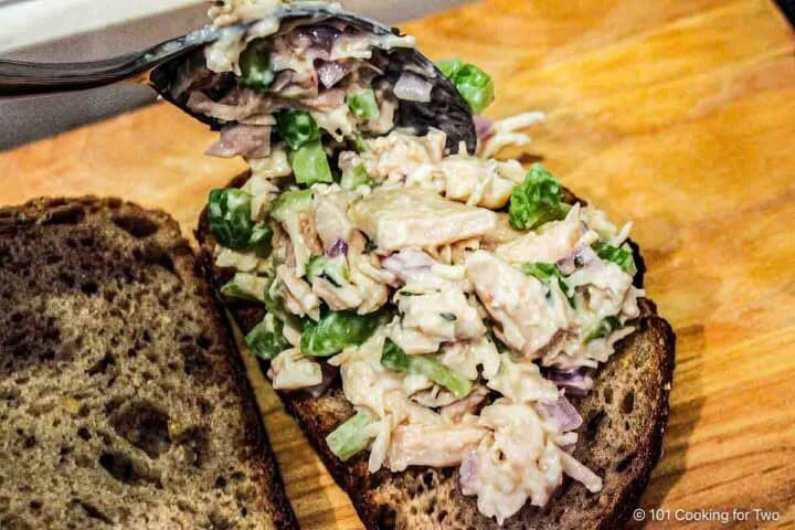 Spooning chicken salad onto sandwich bread.