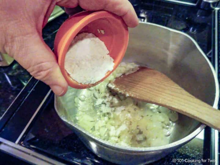 Sprinkling flour into a pan of cooked onion and butter.